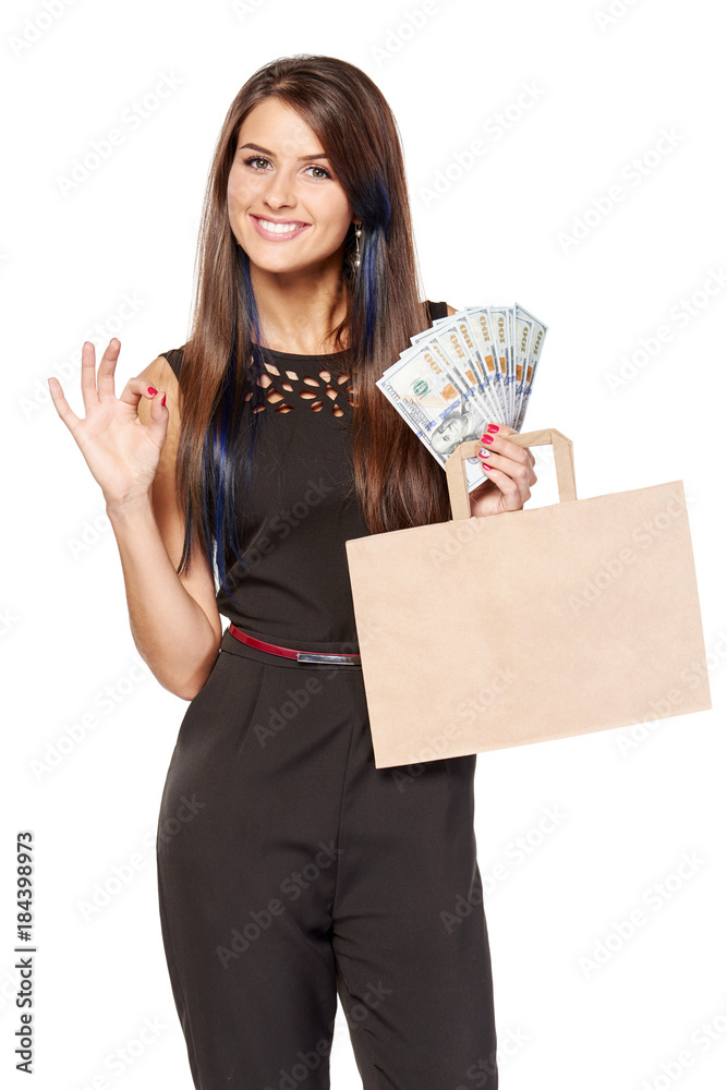 Cash payment approved. Smiling woman holding paper shopping bag with blank copy space for text and cash US dollars while gesturing OK, over white background Cash payment approved. Smiling woman holding paper shopping bag with blank copy space for text and cash US dollars while gesturing OK, over white background