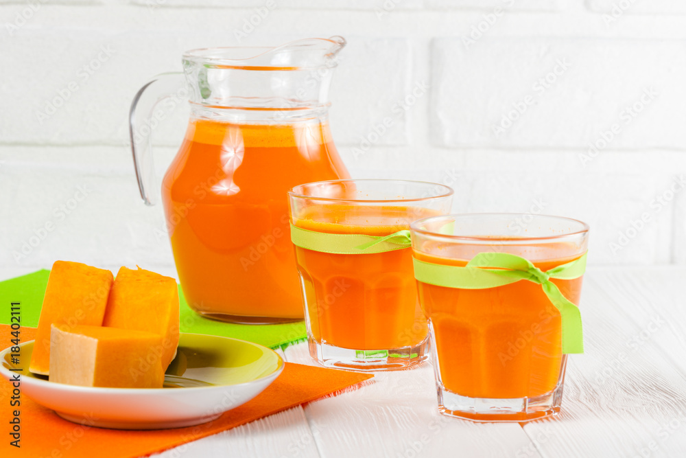 Pumpkin fresh juice in beautiful glasses and jug with pieces of ripe vegetable on white wooden background. Sweet orange juice. Healthy eating, diet theme. Close up photography. Horizontal banner