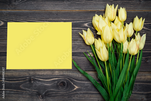 Spring background with yellow tulip flowers and yellow sheet of paper, copy space. Flat lay, top view, horizontal. Holiday greeting card for Valentine's Day, Woman's Day (March 8, Mother's Day, Easter