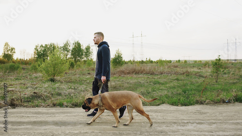 Young sporty man walking with his bullmastiff dog outdoor at nature after crossfit training