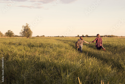 a couple of girls go on a dirt road on the big field with tall grass