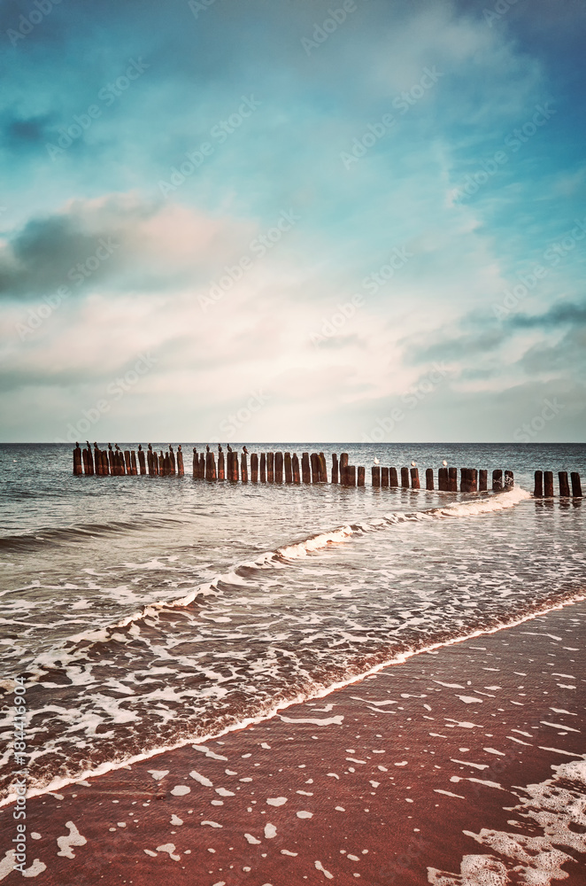 Vintage toned picture of an old wooden breakwater on a beach, nature background.