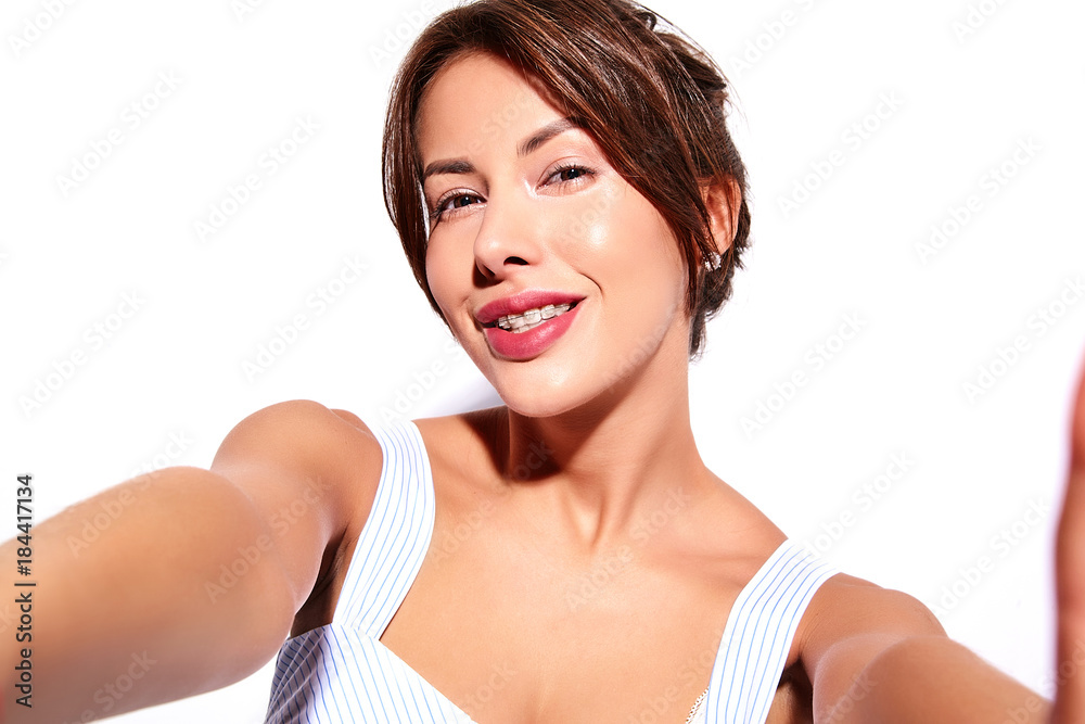 Smiling beautiful cute brunette woman model in casual summer dress with no makeup with white braces on teeth making selfie photo on smartphone, isolated Smiling beautiful cute brunette woman model in casual summer dress with no makeup with white braces on teeth making selfie photo on smartphone, isolated