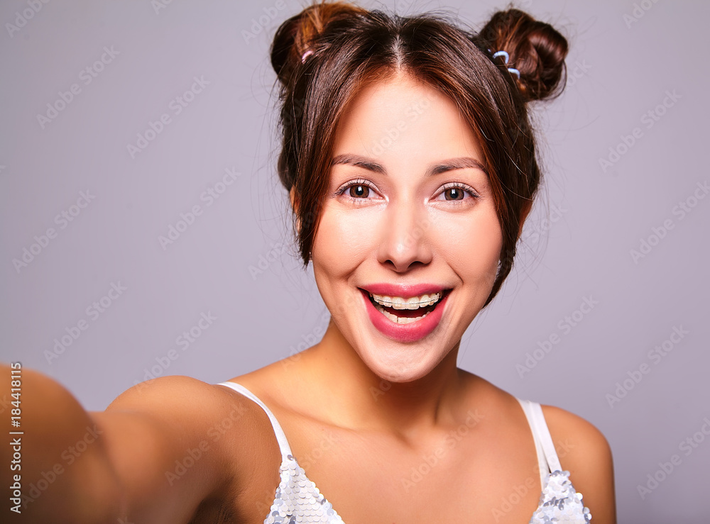 Naklejka premium Portrait of beautiful cute brunette woman model in casual clothes with no makeup making selfie photo on smartphone isolated on gray
