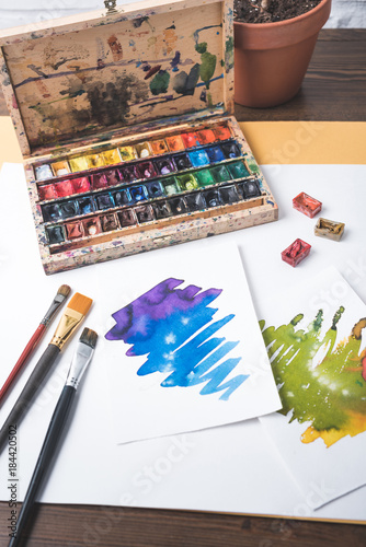 top view of paints, paintbrushes and watercolor sketches at designer workplace