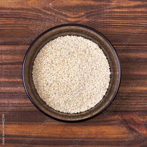 White sesame seeds in a bowl on a wooden background