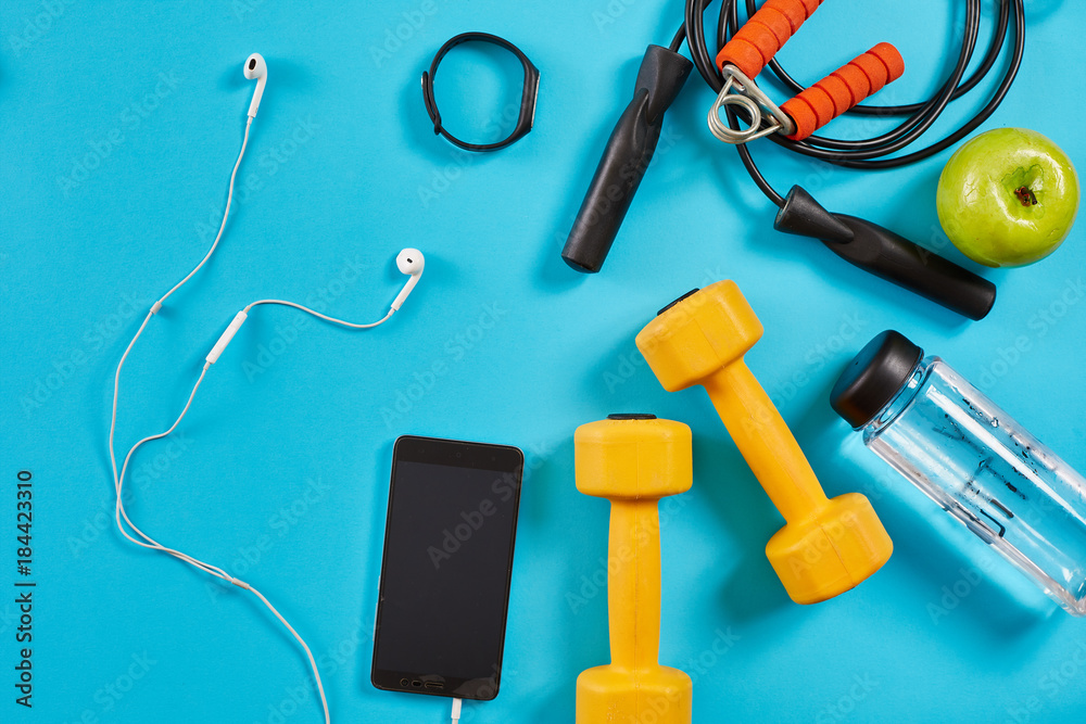 Dumbbells, mobile phone and skipping rope on blue background. Top view. Fitness, sport and healthy lifestyle concept. Dumbbells, mobile phone and skipping rope on blue background. Top view. Fitness, sport and healthy lifestyle concept.
