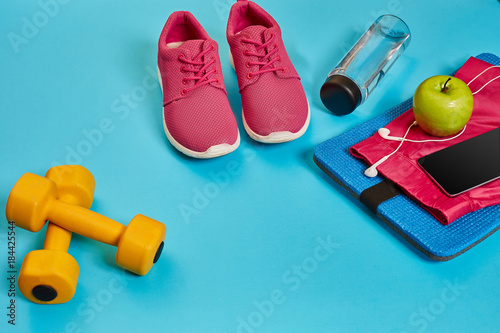 Healthy concept, diet plan with sport shoes and bottle of water and dumbbells on blue background, healthy food and exercise concept © nazarovsergey