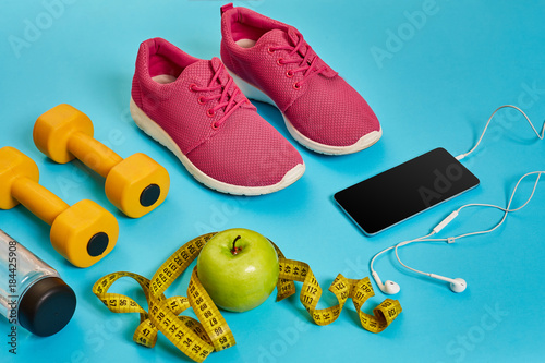 Healthy concept, diet plan with sport shoes and bottle of water and dumbbells on blue background, healthy food and exercise concept