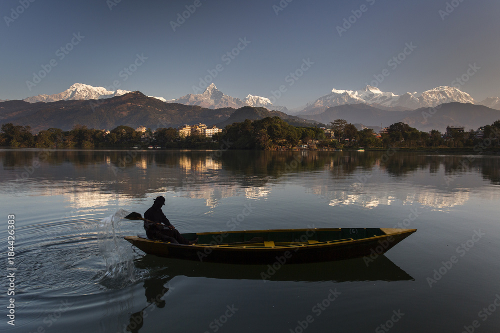 Beautiful landscape with Phewa Lake and boat on lake, mountains in background also as reflectaion on lake.  Machapuchare-FIshtail, Annapurna and many others. Pokhara, Nepal