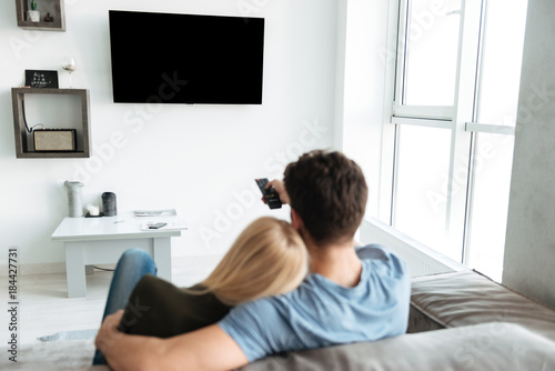 Back view of couple sitting on sofa and watching TV