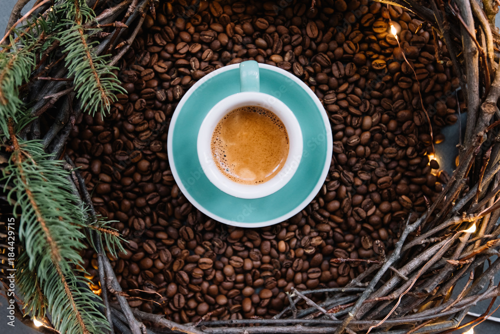 Delicious freshly brewed espresso in a ceramic green cup with saucer, with a beautiful crema, set on coffee beans and with winter festive handmade wooden wreath with fireflies around it, top view Delicious freshly brewed espresso in a ceramic green cup with saucer, with a beautiful crema, set on coffee beans and with winter festive handmade wooden wreath with fireflies around it, top view