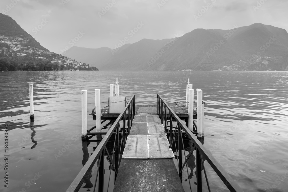 Boat pier on the Lake Lugano, Switzerland. Black and white photography. European vacation, travel and nautical concept.
