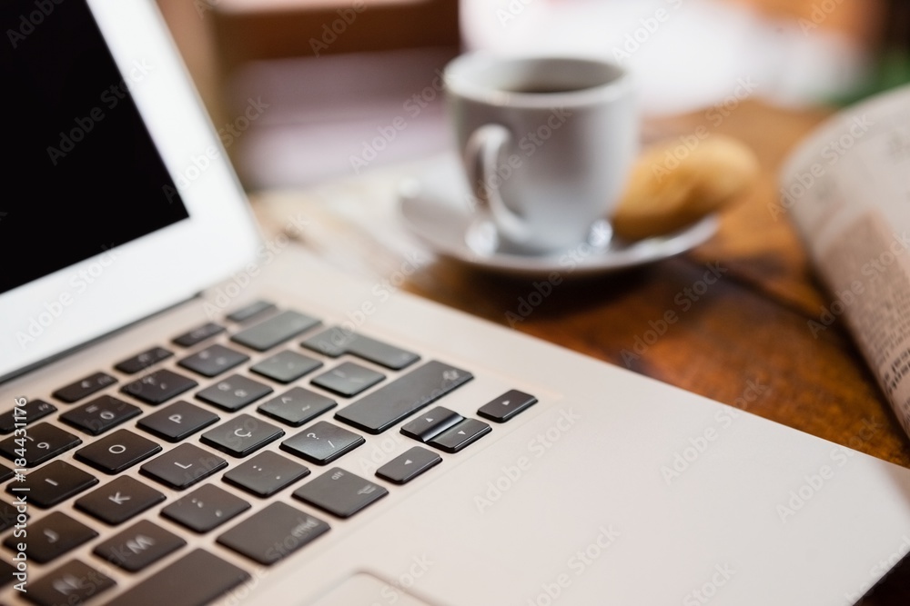 Close up of coffee cup by laptop on wooden table Close up of coffee cup by laptop on wooden table