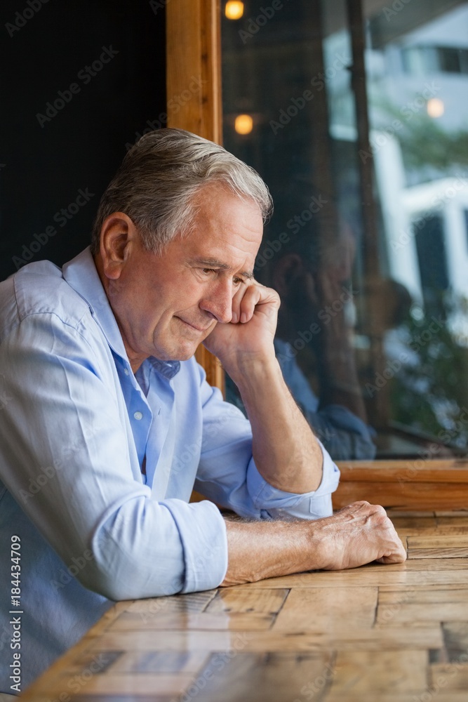 Thoughtful senior man looking away while sitting at table Thoughtful senior man looking away while sitting at table