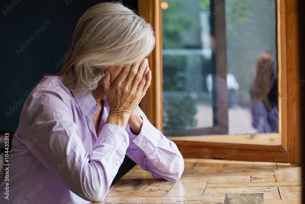 Senior woman covering face while sitting at table in cafe Senior woman covering face while sitting at table in cafe