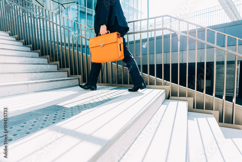 midsection contemporary business man walking upstairs in the city backlight, holding overnight bag - business, work concept