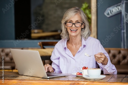 Fotografie Portrait of senior woman using laptop computer while eating