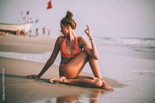young woman in swimsuit practicing yoga on beach at goa