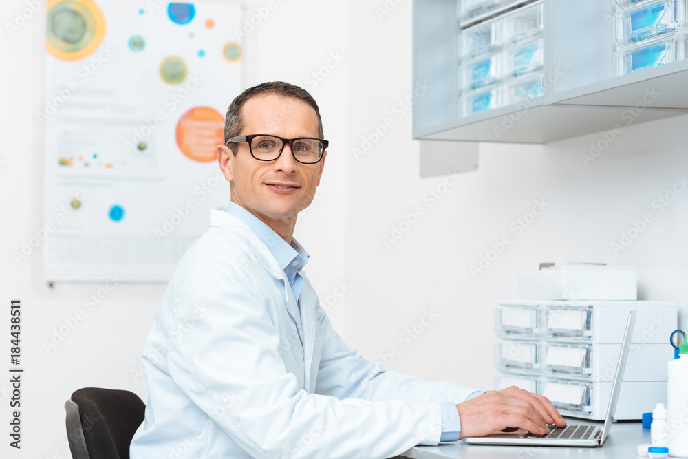 side view of doctor in white coat working on laptop at workplace in clinic side view of doctor in white coat working on laptop at workplace in clinic