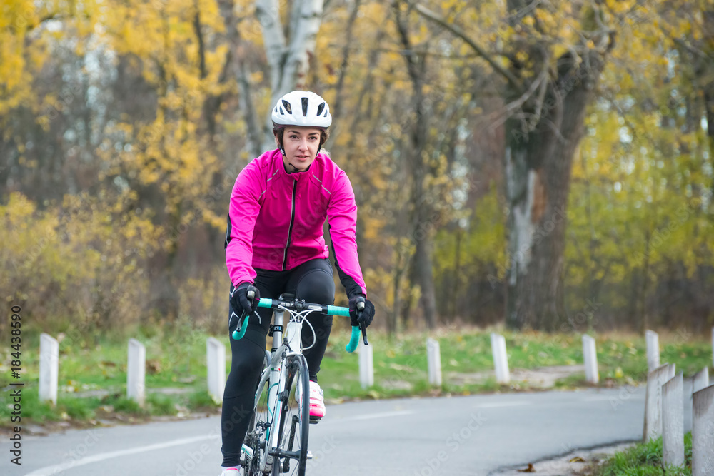 Fototapeta premium Young Woman in Pink Jacket Riding Road Bicycle in the Park in the Cold Autumn Day. Healthy Lifestyle.