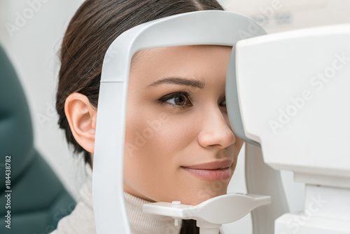 Fotografie side view of young woman getting eye examination in slit lamp in clinic