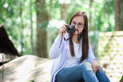 Beautiful girl holding a camera in a garden with a big tree.