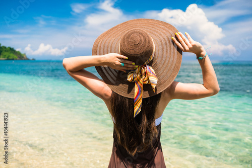 Woman in summer vacation wearing straw hat and beach dress enjoying the view at the ocean