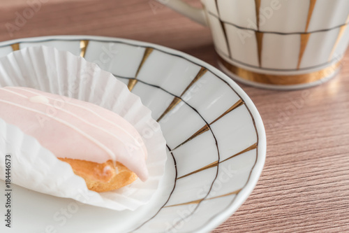 respberry eclair on a plate near tea cup on wooden table photo