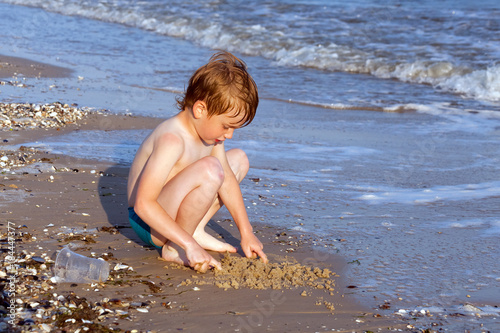 Happy boy having fun on the background of sea playing with sand and water in sunset reys