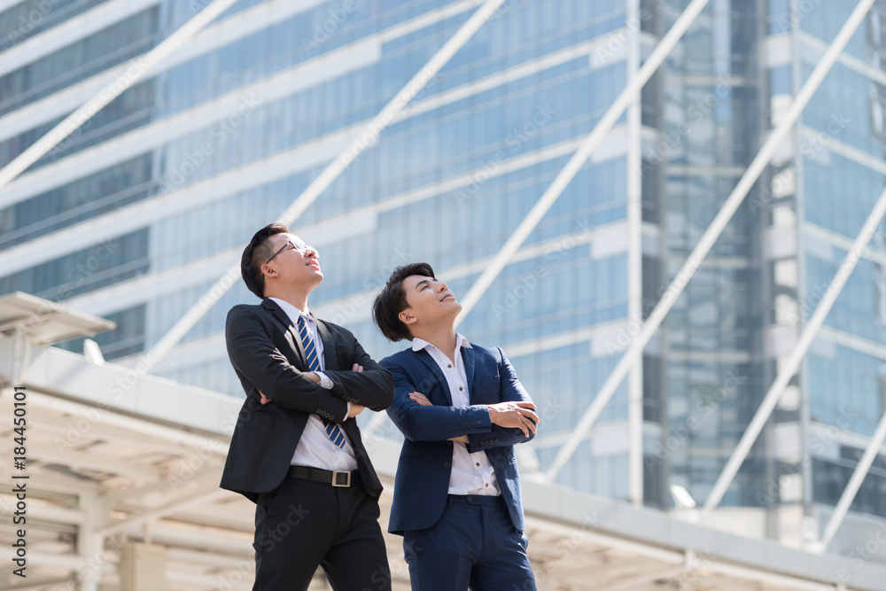 Successful two businessman in suit standing in city with hands crossed on chest, looking go big city buildings, planning new projects, waiting for meeting to start. Copy space for text. Successful two businessman in suit standing in city with hands crossed on chest, looking go big city buildings, planning new projects, waiting for meeting to start. Copy space for text.