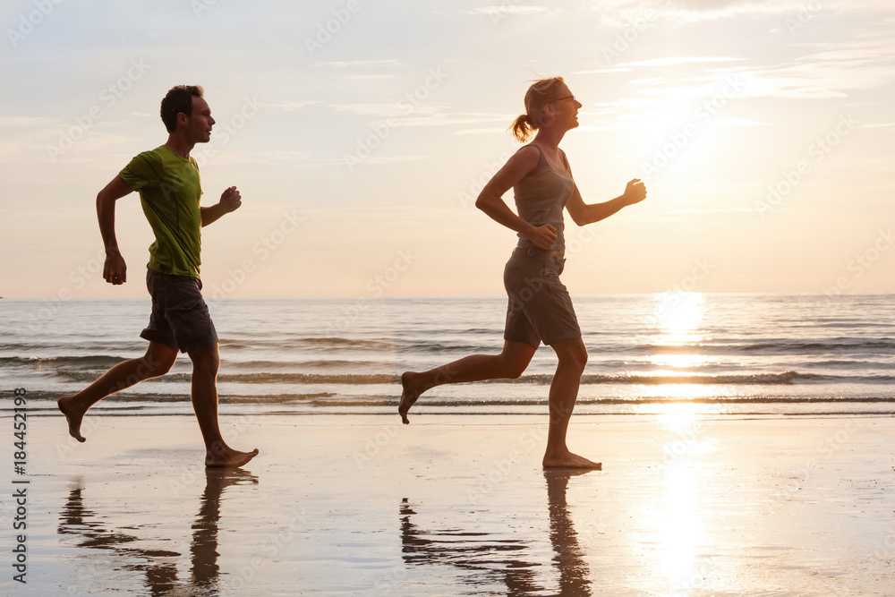Happy young couple jogging on beautiful sunset sea beach. Sporty lifestyle concept.