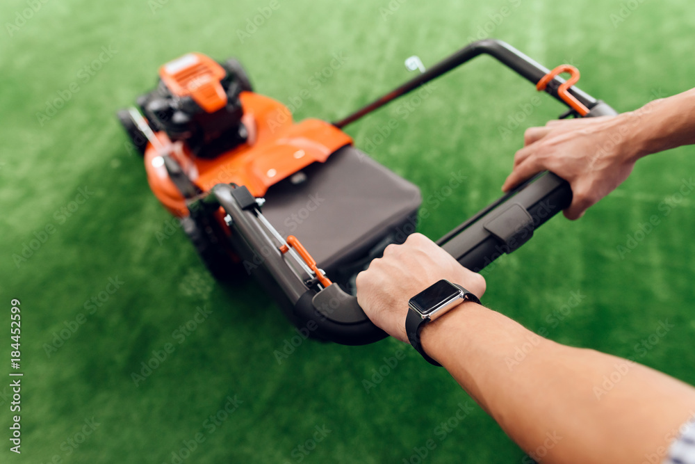 A man holds a lawn mower for the handle. A man holds a lawn mower for the handle.