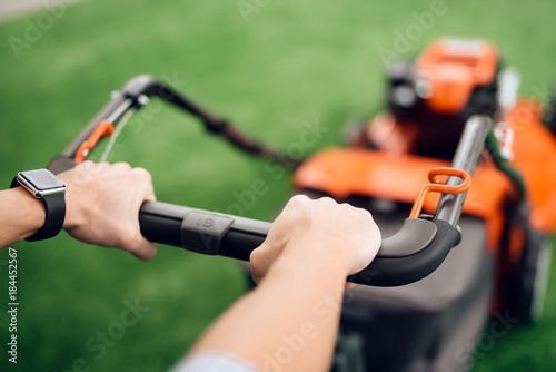 A man holds a lawn mower for the handle.