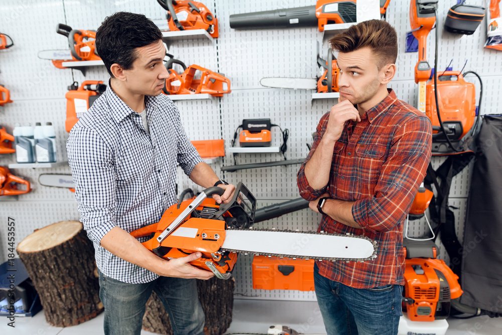 The seller in the store shows the customers a chainsaw. The seller in the store shows the customers a chainsaw.
