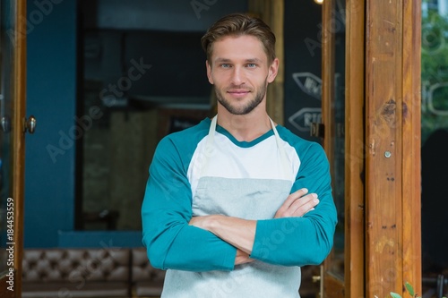 Portrait of smiling waiter standing with arms crossed