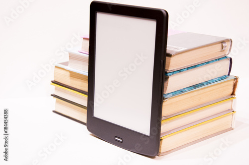 E-book stands next to paper books. New paper technologies. Replacing paper books. Convenience and comfort of reading. White background. Isolated.