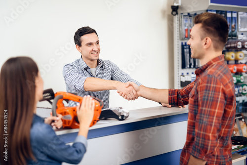Obraz na plátně The guy and the girl pay for the purchase of a chainsaw.