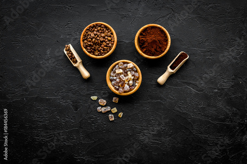 Coffee background. Roasted beans, ground coffee and sugar in bowls and scoops on black table top view copyspace