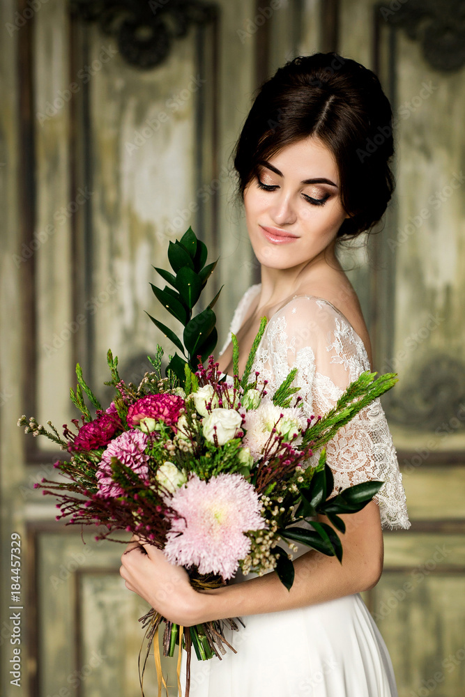 Bride in white dress sitting on chair indoors in dark studio interior like at home.