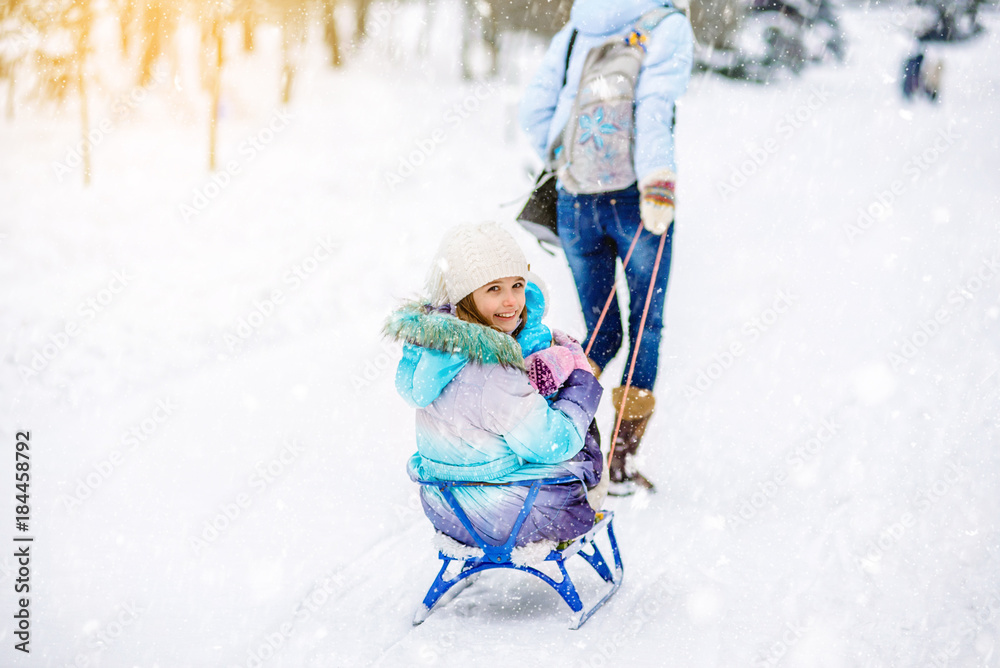 Mom rolls her little daughter on the sled in winter Mom rolls her little daughter on the sled in winter