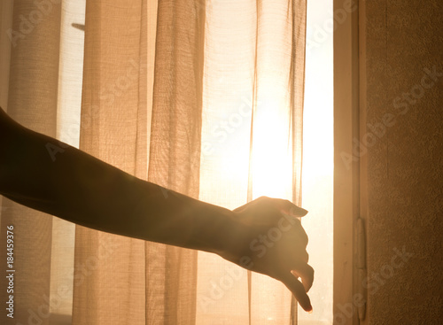 Female arm reaching out to open a curtain - warm sun light shining through