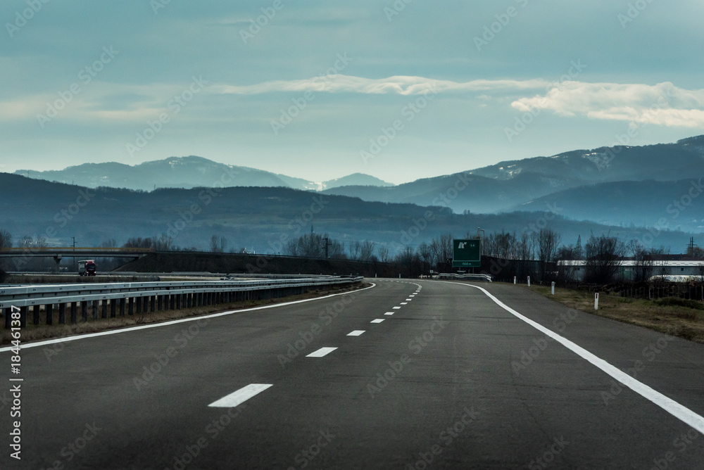 Two line wide highway on a cloudy winter day leading to the mountains through rural landscape Two line wide highway on a cloudy winter day leading to the mountains through rural landscape