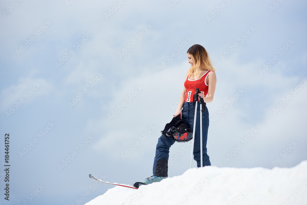 Young woman skier wearing ski pants and red swimsuit, standing on the top of the snowy hill with ski equipment at winter ski resort copyspace sport seasonal sportspeople adrenaline extreme concept Young woman skier wearing ski pants and red swimsuit, standing on the top of the snowy hill with ski equipment at winter ski resort copyspace sport seasonal sportspeople adrenaline extreme concept