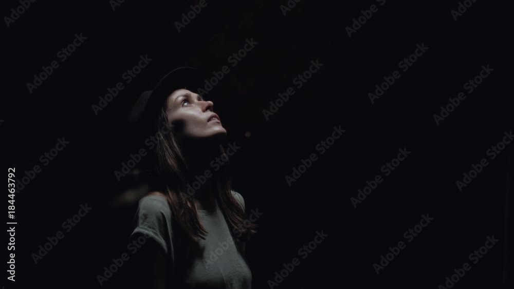 female with a black cap stands in a dark cave looking up at the light in the sky female with a black cap stands in a dark cave looking up at the light in the sky