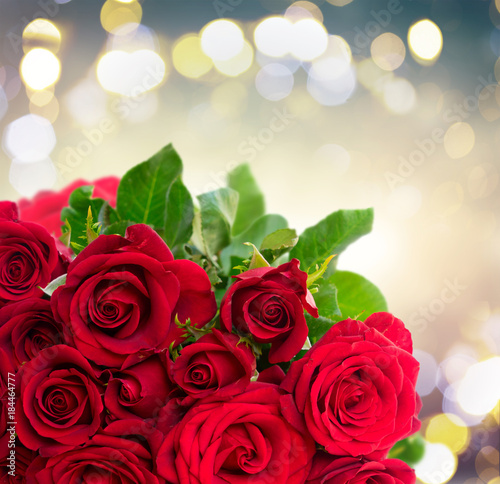 Bouquet of dark red rose buds with green leaves close up on festive bokeh background