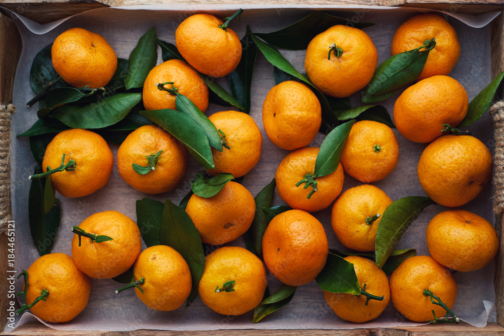 Many small tangerine with leaves in a wooden box top view