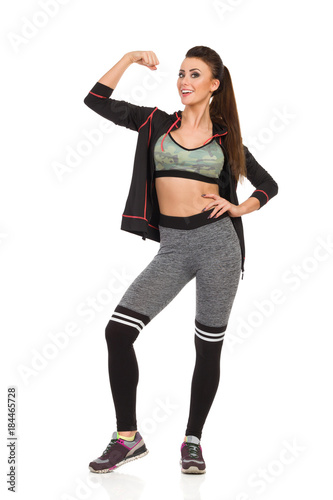 Fit Smiling Young Woman Is Rising Arm And Flexing Muscle