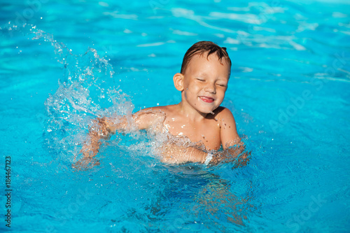 Happy kid playing in blue water of swimming pool. Little boy learning to swim. Summer vacations concept. Cute boy swimming in pool water. Child splashing in swimming pool © nata_zhekova