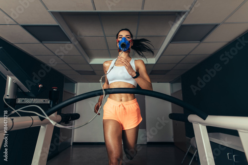 Fit woman running on treadmill with a mask